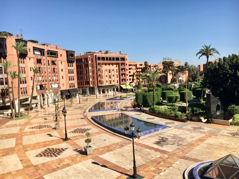 Marrakech's modern Gueliz district, featuring broad streets, pink-hued buildings, landscaped gardens, and a reflective water feature.
